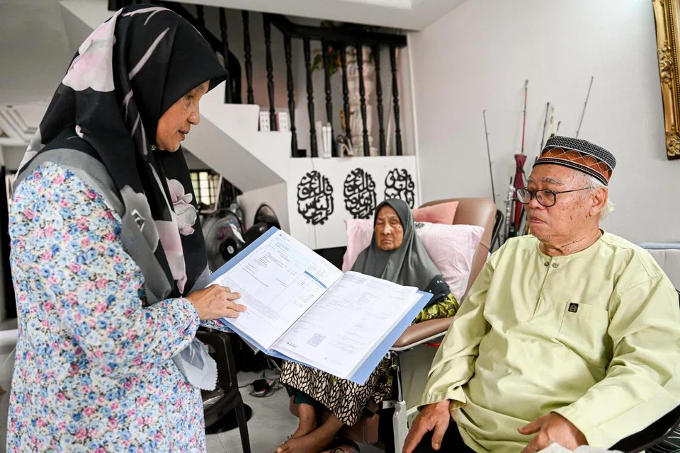 Cik Fareha Mohd Jaafar (kiri) menunjukkan resit perubatan ibunya, Cik Aminah Puteh (tengah), yang mencecah sehingga $100 seminggu. Bersama mereka ialah suami Cik Fareha, Encik Mohamad Rihat Mohamad Tahir.