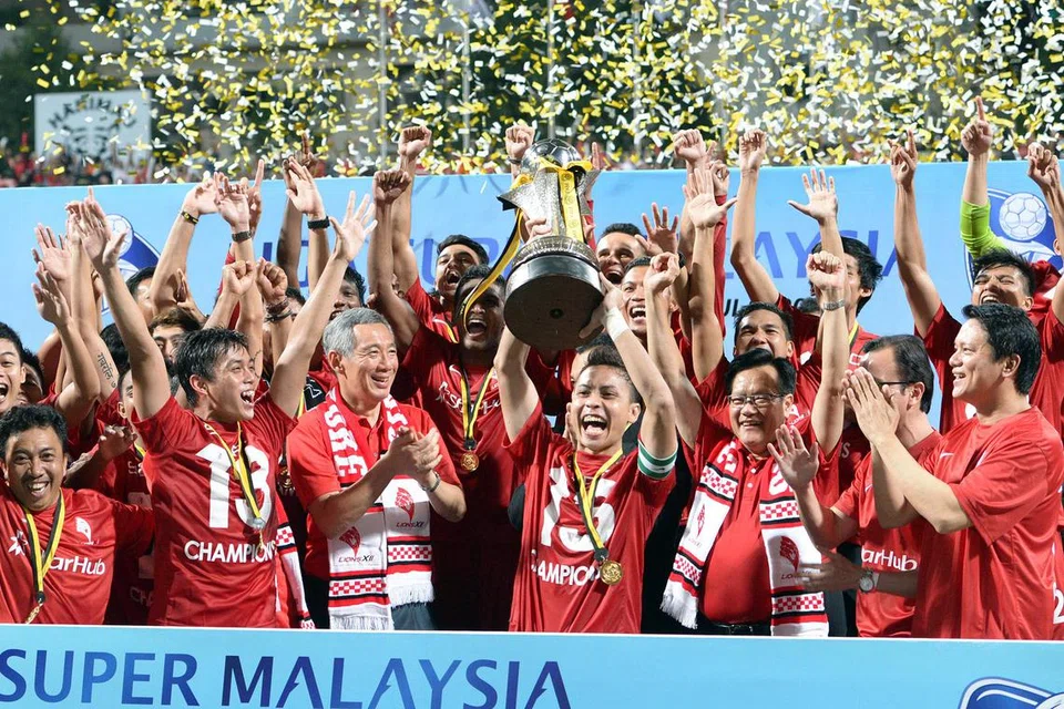 (barisan depan, menjulang trofi) Shahril Ishak, bekas kapten pasukan bola sepak nasional Singapura, meraikan kejuaraan pasukan LionsXII dalam Liga Super Malaysia 2013 bersama Encik Lee Hsien Loong (di kanannya). 