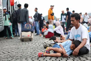 A boy lies down on his father's lap as they wait to depart on a bus that the Jakarta Provincial Government has arranged for free of cost as people return to their hometowns, known locally as "mudik", ahead of the Eid al-Fitr celebration, at the National Monument in Jakarta, Indonesia, March 27, 2025. REUTERS/Ajeng Dinar Ulfiana