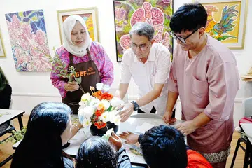 Pemangku Menteri Bertanggungjawab bagi Ehwal Masyarakat Islam, Profesor Madya Dr Muhammad Faishal Ibrahim (dua dari kiri), bersama Setiausaha Kehormat HGEF, Cik Haslinda Putri Harun (kiri) dan pencipta kandungan gaya hidup Bob Mubarak (kanan), menyaksikan Cik Siti (bawah kiri) menggubah bunga bersama anak-anak semasa acara Projek Pelita Hati 2026 di Kamal Arts Studio di Wisma Geylang Serai pada 14 Mac.