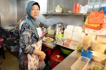 SELERA MAKANAN MELAYU: Cik Raya (gambar atas) menyiapkan makanan yang dipesan para pelanggannya. - Foto ZAINAL YAHYA 