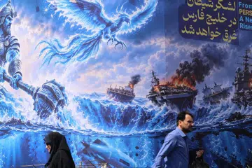 Penduduk Iran melintasi papan iklan besar anti-Amerika Syarikat bertulis “Tentera syaitan akan ditenggelamkan di Teluk Parsi” di Dataran Enghelab, Tehran, pada 14 September 2026. Perang Amerika-Iran dianggarkan sudah menelan belanja sekurang-kurangnya AS$33.4 bilion bagi Washington, selain menyebabkan kekurangan beberapa jenis amunisi dan kerosakan besar pada aset tenteranya di Asia Barat.
