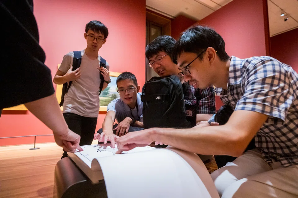 Seorang kakitangan Jabatan Komuniti & Akses memimpin sekumpulan peserta dengan pelbagai ketidakupayaan, menggunakan buku dengan penekanan pada unsur sentuhan, daripada koleksi, ‘Hands On Learning and Development’ (Hold).