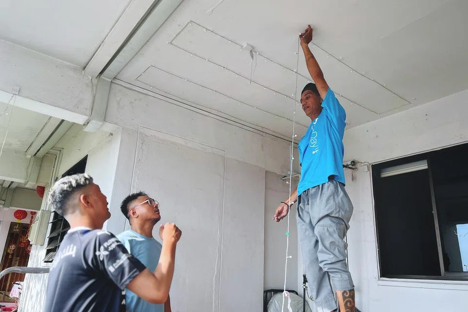 Encik Farid Difari, 46 tahun (kanan) yang terkenal atas lampu lap-lip viral di Chong Pang, kelihatan memasang lampu lap-lip bagi jirannya Encik Syahril Omar Taib, 35 tahun (kedua dari kiri) dan dibantu adiknya Encik Faizal Difari, 36 tahun.