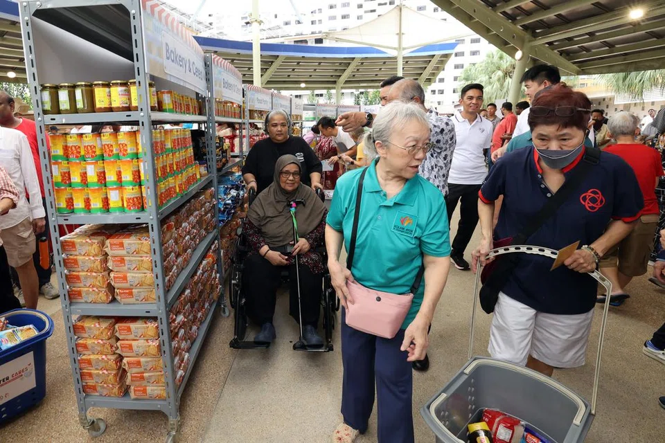 PERKASA PENDUDUK: Cik Saerah Sapet (duduk di kerusi roda) boleh mengambil barang runcit pilihannya menerusi usaha bantuan Kolam Ayer Cares yang dijalankan bak di pasar raya. 