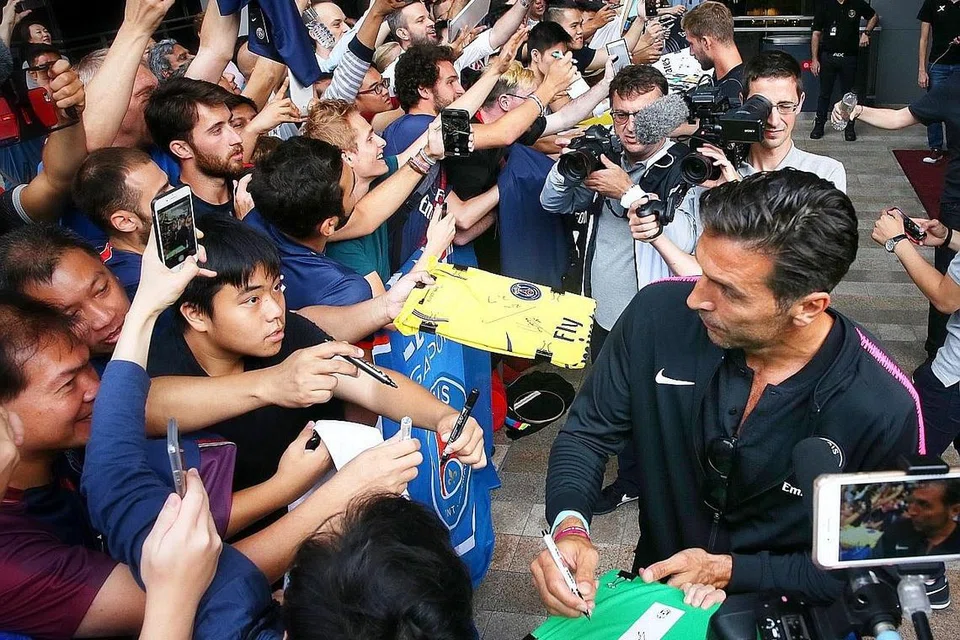 JADI TARIKAN: Penjaga gawang Gianluigi Buffon (kanan) bergambar dan memberi autograf kepada peminat yang menantinya di Hotel JW Marriot Singapore South Beach sedang pasukan Paris Saint Germain (PSG) tiba untuk perlawanan Piala Juara-Juara Antarabangsa (ICC). Pemain berusia 40 tahun ini menjadi tarikan selepas peminat kecewa apabila bintang muda seperti Neymar dan Kylian Mbappe tidak hadir kerana terlibat dalam Piala Dunia. - Foto BM oleh GAVIN FOO