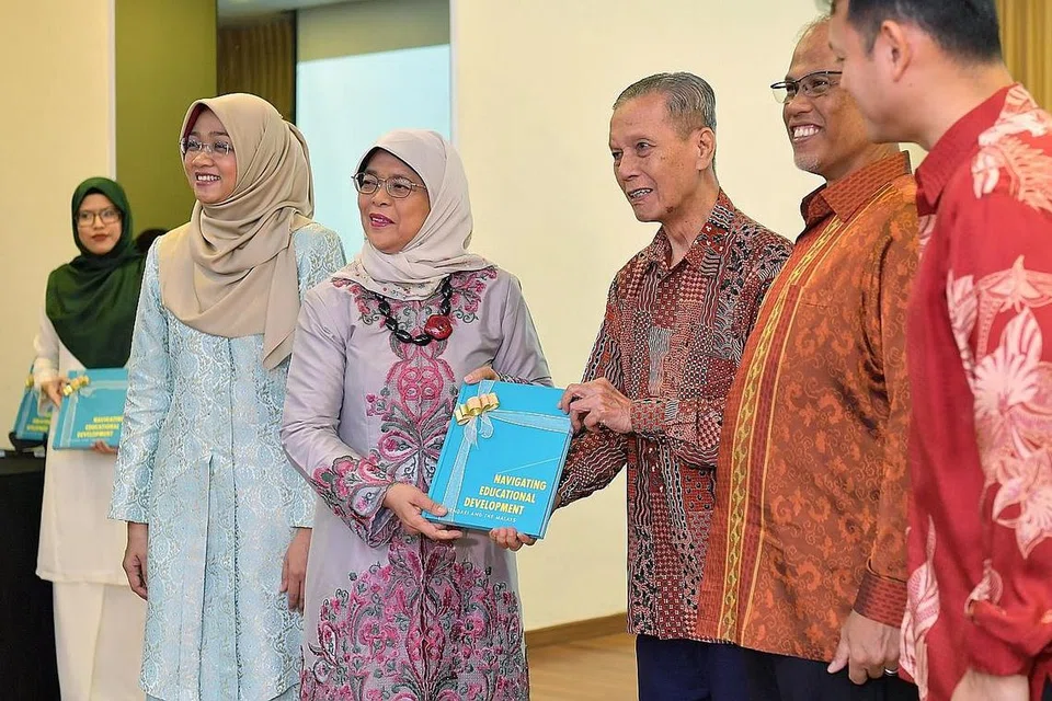 TANDA PENGHARGAAN: Presiden Halimah menyampaikan buku peringatan Navigating Educational Development: Mendaki and the Malays kepada Haji Shafawi Ahmad, anggota pengasas Mendaki sambil disaksikan (dari kanan) Encik Zaqy dan Encik Masagos serta Cik Rahayu (dua dari kiri). - Foto BH oleh NG SOR LUAN
