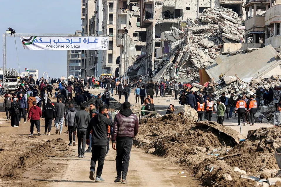 Penduduk Gaza dilihat berkumpul berhampiran kain rentang yang mengalu-alukan kepulangan penduduk berhampiran runtuhan bangunan di sepanjang Jalan al-Rashid, Gaza, pada 26 Januari. Lokasi ini menjadi laluan bagi mereka yang melintasi Koridor Netzarim, yang sebelum ini disekat oleh Israel, dari bahagian selatan Gaza menuju ke Bandar Gaza.