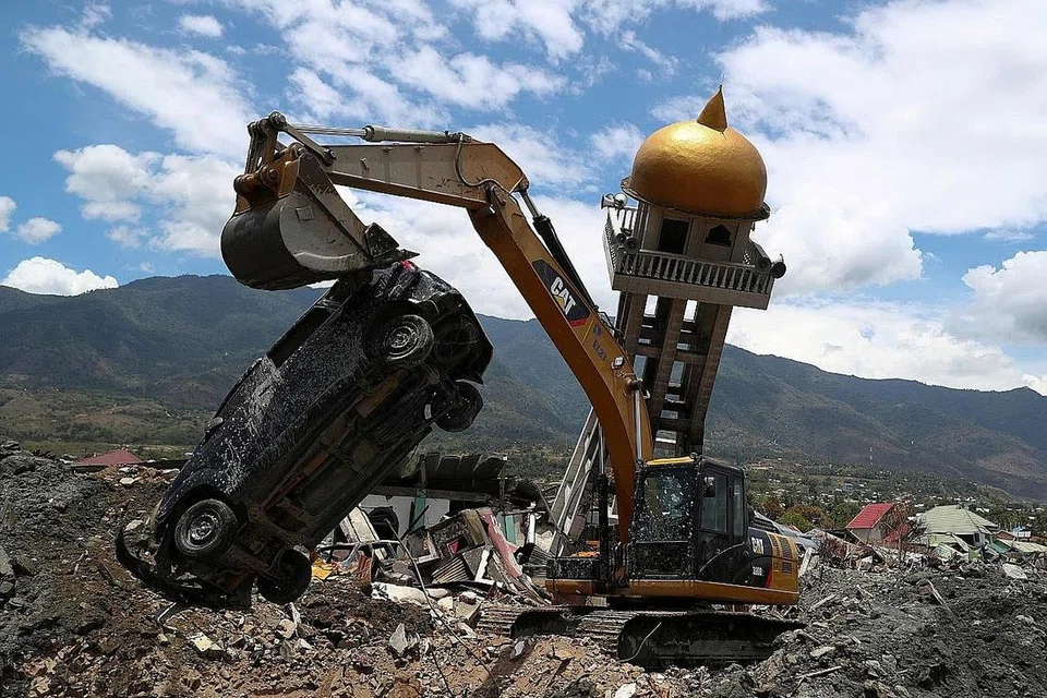 KERJA-KERJA PEMULIHAN: Mesin pengorek memindahkan sebuah kereta yang rosak bersebelahan sebuah masjid yang rosak akibat gempa bumi di kawasan kejiranan Balaroa, Palu, Sulawesi. - Foto REUTERS