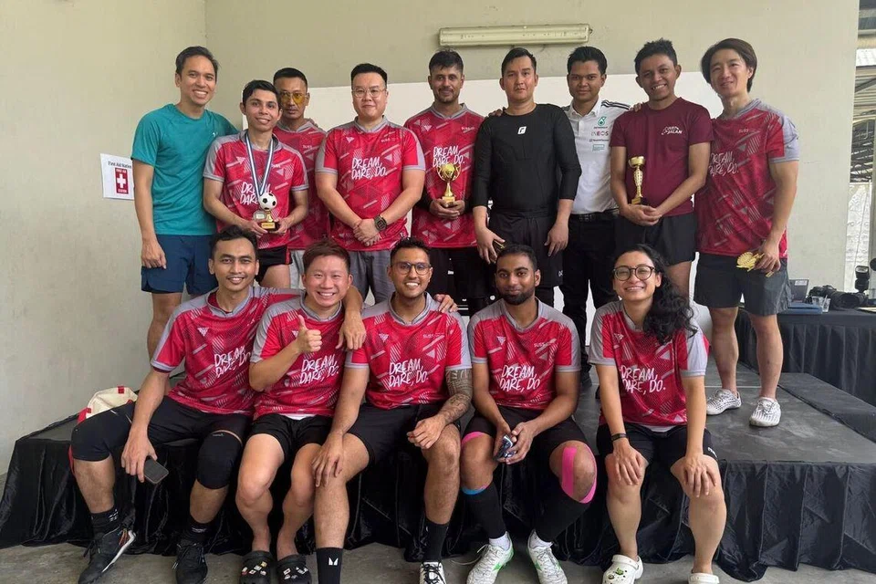 Encik Nabil (barisan depan, tengah) dan rakan daripada pasukan futsal Universiti Sains Kemasyarakatan Singapura (SUSS) menyertai kejohanan amal tahunan, Piala Ketua Hakim Negara 2025, yang menghimpunkan kakitangan guaman bagi mengumpul dana untuk Dana Reben Kuning (YRF) dan Persatuan Penjagaan Lanjut Singapura (Saca).