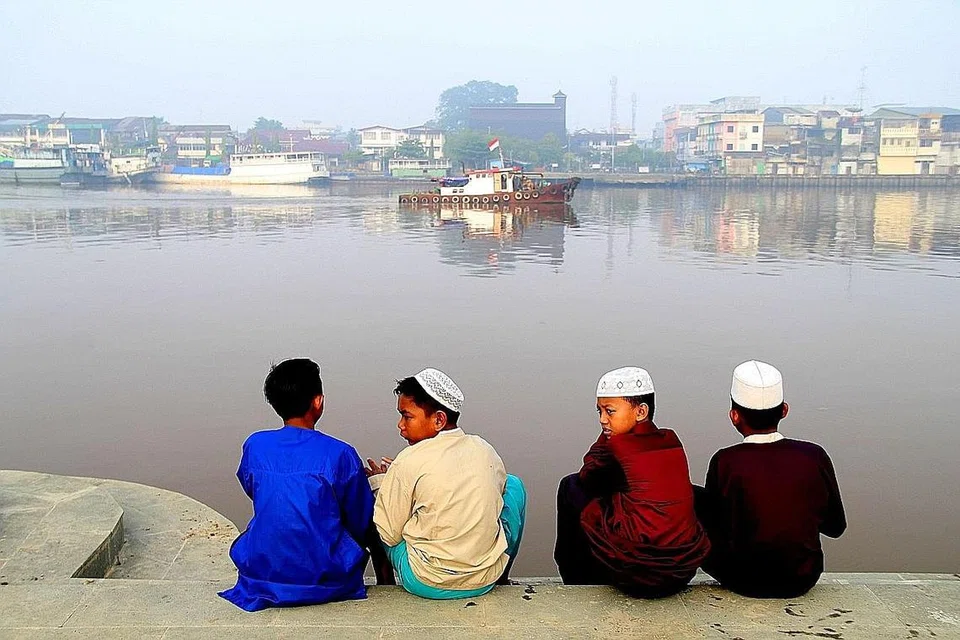 DISELUBUNGI JEREBU: (Gambar kanan) Kanak-kanak duduk di tebing Sungai Kapuas sedang jerebu melanda bandar Pontianak, Kalimantan Barat. - Foto Reuters
