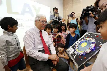 SENTUHAN REALITI: Presiden Tony Tan Keng Yam beramah-tamah bersama kanak-kanak di Akademi Pembelajaran Prasekolah, atau Play@TP, yang antara lain membolehkan pelajar kursus Pendidikan Awal Kanak-Kanak Politeknik Temasek memperolehi pengalaman sebenar dalam 'tadika eksperimen'. - Foto THE STRAITS TIMES