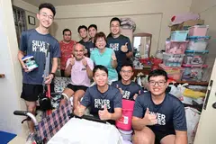 HARGAI BANTUAN: Encik Muhammad Imran Abdullah, 58 tahun (duduk, berbaju ungu), yang kini tidak dapat berjalan tanpa bantuan, bersama Mayor Majlis Pembangunan Masyarakat (CDC) Central Singapore, Cik Denise Phua (berbaju biru pirus), dan anggota Angkatan Bersenjata Singapura (SAF).