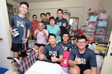 HARGAI BANTUAN: Encik Muhammad Imran Abdullah, 58 tahun (duduk, berbaju ungu), yang kini tidak dapat berjalan tanpa bantuan, bersama Mayor Majlis Pembangunan Masyarakat (CDC) Central Singapore, Cik Denise Phua (berbaju biru pirus), dan anggota Angkatan Bersenjata Singapura (SAF).