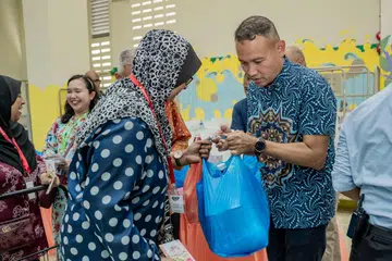 AGIH DAGING KORBAN: Mayor Majlis Pembangunan Masyarakat (CDC) South East, Encik Mohd Fahmi Aliman (kanan) mengagihkan daging korban kepada penerima bantuan di Rumah Peralihan Pertapis pada Sabtu.
