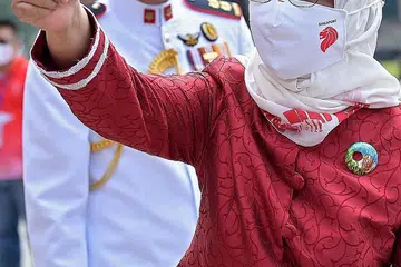 MERAH PUTIH: Presiden Halimah Yacob (gambar kanan), yang menggayakan kerongsang enamel dan selendang putih yang rekaannya mendapat inspirasi daripada hasil seni artis kurang upaya dan dicipta bersama jenama setempat di bawah inisiatif SG Enable, memberi isyarat jempol kepada penonton setibanya di Padang semalam. - Foto-foto BH oleh NG SOR LUAN.