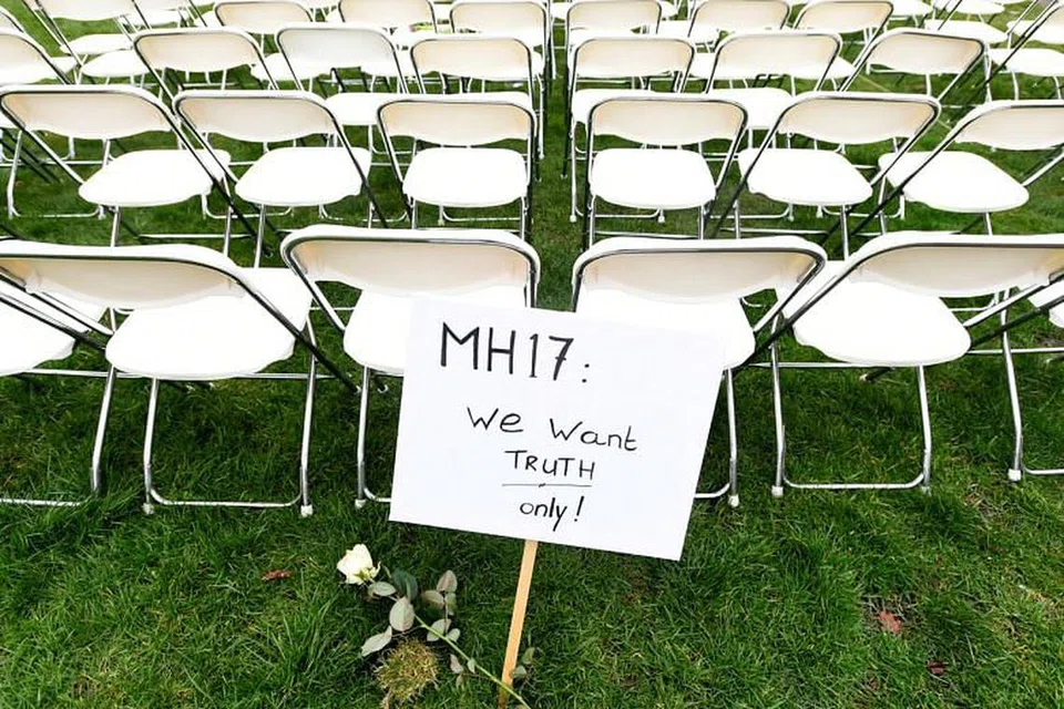 Satu tanda bantahan berhampiran deretan bangku sedang keluarga mangsa MH17 mengatur bangku kosong bagi setiap tempat duduk dalam pesawat dalam satu bantahan di luar Kedutaan russia di The Hague, Netherlands, pada 8 Mac. 