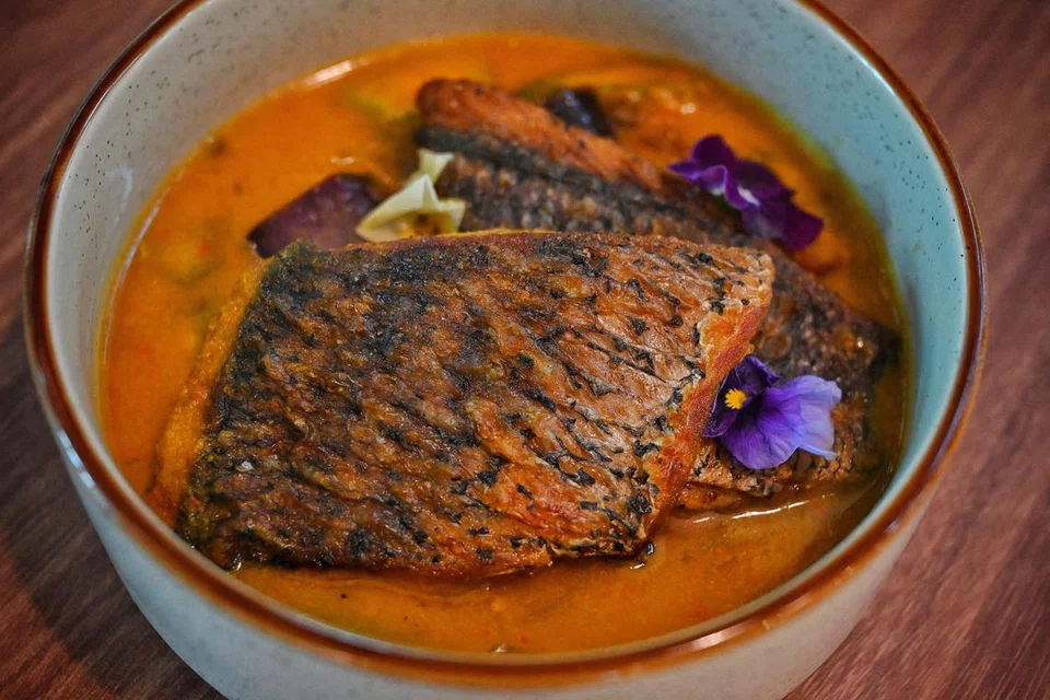 Nyonya Assam Barramundi dihidangkan bersama nasi kuning dan acar berharga $21.80, menggabungkan rasa masam yang segar serta pedas.
