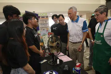 Menteri Kanan, Encik Lee Hsien Loong (dua dari kanan), berinteraksi dengan penuntut tahun pertama jurusan Robotik dan Mekatronikdi Politeknik Nanyang (NYP) Nathan Ian, 17 tahun (tiga dari kiri) semasa lawatannya ke reruai ‘Repair Kopitiam’ di acara Eco Fest anjuran bersama pertubuhan akar umbi Teck Ghee dan NYP berlangsung di Kelab Masyarakat Teck Ghee pada 3 November.