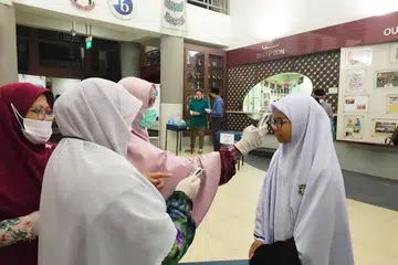 AWASI KEADAAN: Kakitangan Madrasah Aljunied Al-Islamiah sedang mengambil suhu badan pelajar secara beramai-ramai sebelum kelas bermula. - Foto FACEBOOK/ MADRASAH ALJUNIED AL-ISLAMIAH