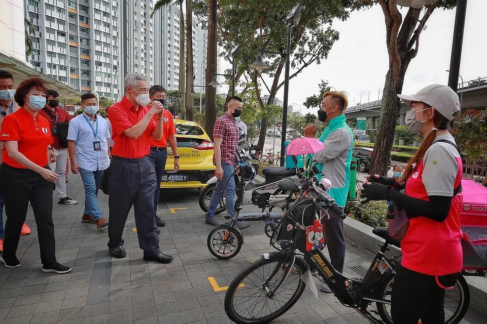 SELAMAT TAHUN BARU: Encik Lee, yang diiringi Presiden NTUC, Cik Mary Liew (paling kiri) dan Setiausaha Agung NTUC, Encik Ng Chee Meng (berbaju merah, di kiri Encik Lee) mengucapkan Selamat Tahun Baru Cina kepada penunggang penghantaran, Encik Raymond Tan dan Cik Cindy Goh.