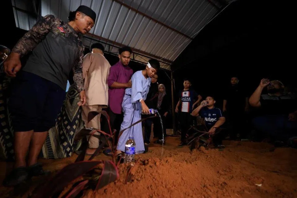 Farouq, 12 tahun (kanan) iaitu anak bongsu Allahyarham Hasnatul Adilah Hassan, 48 tahun, yang maut dalam nahas jalan raya bas bersama treler di Rompin, Pahang, menyiram pusara ibunya yang dikebumikan di Tanah Perkuburan Islam Jalan Tangki Air dekat Ramuan China Besar, Melaka.