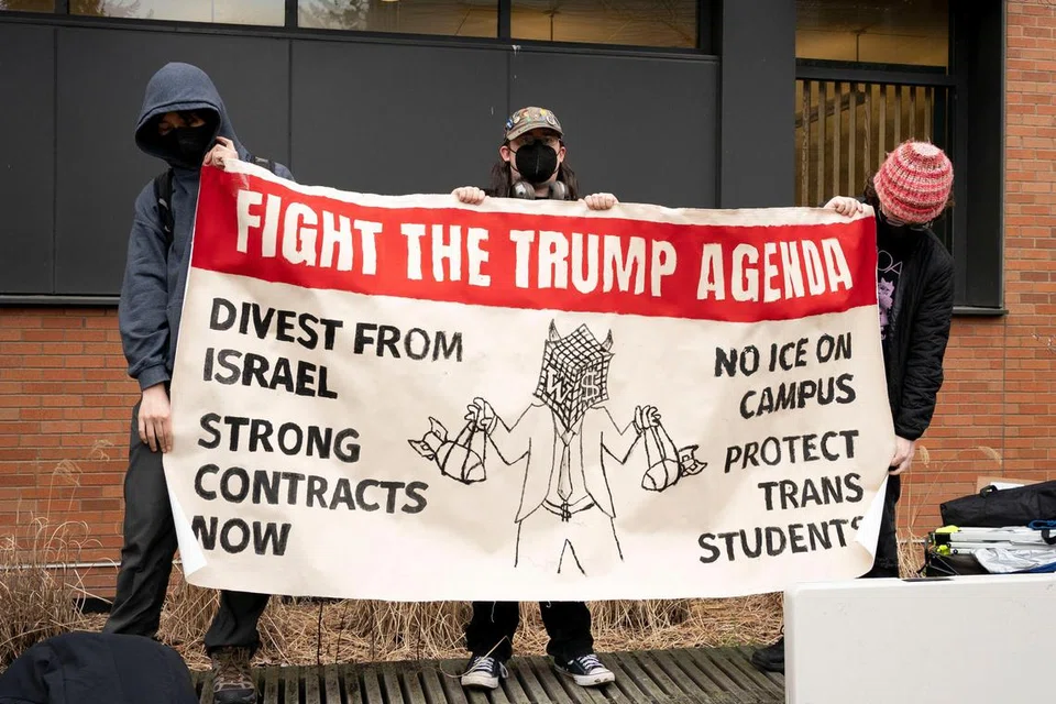 Penunjuk perasaan memegang sepanduk membantah pentadbiran Presiden Amerika Syarikat, Donald Trump, semasa satu demonstrasi yang menyokong pelbagai isu termasuk solidariti terhadap Palestin, imigresen, hak pekerja, dan alam sekitar di Universiti Washington, Seattle, Washington, Amerika Syarikat, pada 12 Mac 2025.