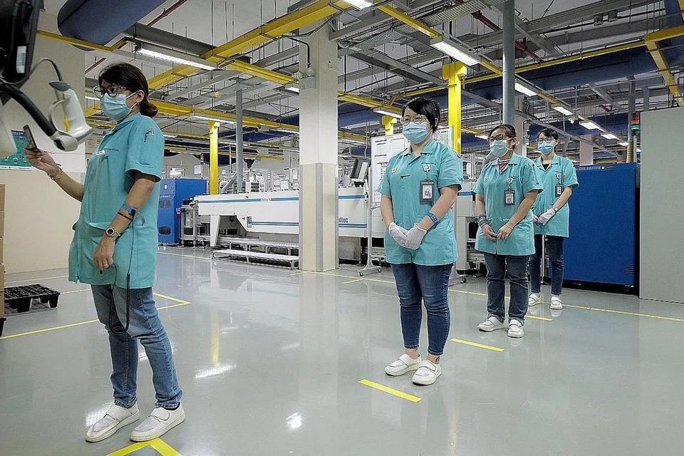 LEBIH RAMAI PEKERJA BUKAN PMET DI INDUSTRI TERJEJAS COVID-19: Pekerja menjaga jarak selamat sambil membuat catatan masuk dan keluar di kilang PepperL + Fuchs di Ayer Rajah Mei lalu. Industri lebih terjejas oleh Covid-19 mempunyai jumlah pekerja bukan PMET lebih tinggi. - Foto fail
