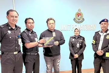 Warga Singapura, Encik Tan Zheng Guang (tengah), bersama pegawai imigresen yang membantu mengembalikan begnya.