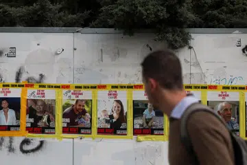 Seorang lelaki melintas di hadapan poster tebusan Encik Yarden Bibas dan dua anaknya, Shiri Bibas dan Kfir Bibas, yang dipasang di tepi jalan raya di Baitulmakdis.