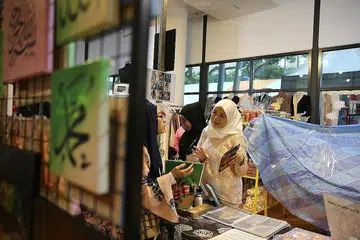 PASAR LAMBAK: Cik Nurlida Yusof (tudung putih) meninjau pasar lambak anjurannya di Wisma Geylang Serai. - Foto BH oleh BENJAMIN SEETOR