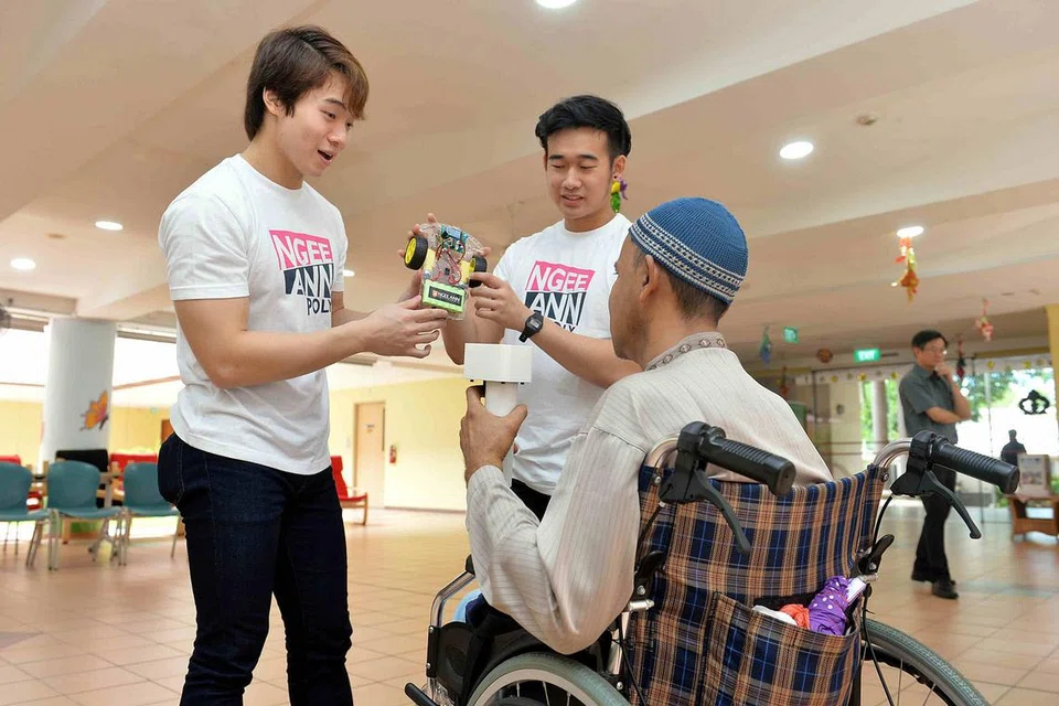 BANTU PESAKIT: Pesakit angin ahmar, Encik Abdul Rahim Abdullah, seronok melakukan fisioterapi kerana dapat mengawal kereta mainan Bluetooth ciptaan penuntut Politeknik Ngee Ann, antaranya Encik Liu (kiri) dan Encik Low (kanan). - Foto M.O. SALLEH