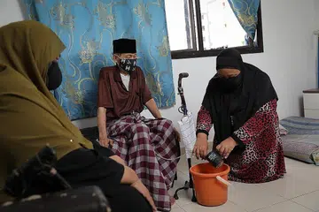 DEMI ORANG TUA: Cik Rozanah (kanan) membantu ayahnya membasuh tiub dan beg yang digunakan untuk membuang air kecil dan mengalihkannya ke sebuah baldi. Turut bersama dalam gambar ialah ibunya. - Foto BH oleh ONG WEE JIN 