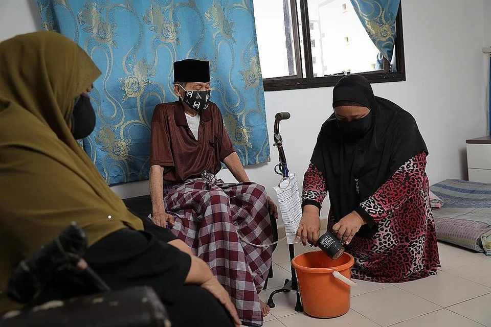 DEMI ORANG TUA: Cik Rozanah (kanan) membantu ayahnya membasuh tiub dan beg yang digunakan untuk membuang air kecil dan mengalihkannya ke sebuah baldi. Turut bersama dalam gambar ialah ibunya. - Foto BH oleh ONG WEE JIN 