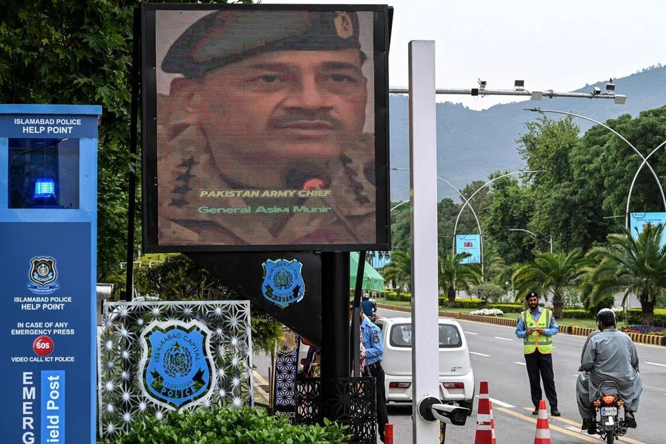 Anggota polis berkawal sambil memeriksa kenderaan di sekatan jalan raya di kawasan Zon Merah, berhampiran skrin besar yang memaparkan Ketua Tentera Pakistan dan Marsyal Syed Asim Munir di Islamabad pada 18 April 2026. Ketua tentera berpengaruh Pakistan itu dan perdana menterinya pada hari yang sama menamatkan lawatan berasingan bagi usaha menamatkan perang Iran, dengan Marsyal Asim Munir berlepas dari Tehran manakala Perdana Menteri Shehbaz Sharif pulang dari Turk