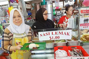 KEKALKAN HARGA, CEPAT LARIS: Cik Zaliah (kiri) menggajikan empat pembantu bagi melayan pelanggan yang gemar nasi lemak $1 di gerainya di mana beliau boleh menjual lebih 300 bungkus pada hari biasa dan sekitar 500 bungkus pada hujung minggu. - Foto BM oleh SAINI SALLEH
