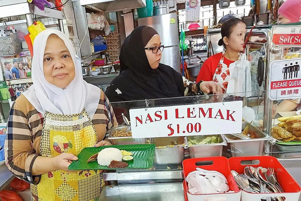 KEKALKAN HARGA, CEPAT LARIS: Cik Zaliah (kiri) menggajikan empat pembantu bagi melayan pelanggan yang gemar nasi lemak $1 di gerainya di mana beliau boleh menjual lebih 300 bungkus pada hari biasa dan sekitar 500 bungkus pada hujung minggu. - Foto BM oleh SAINI SALLEH