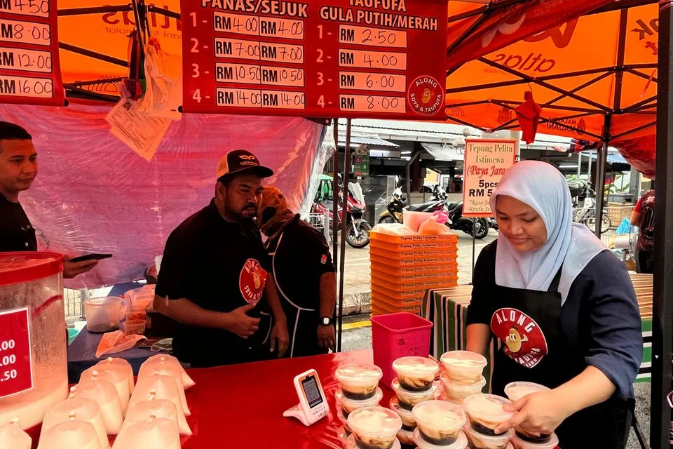 Peniaga air soya dan tau fu faa, Encik Muhammad Khairuddin Mohamad Nasid, 40 tahun (tengah), tidak menang tangan melayan pelanggan di gerainya di bazar Ramadan Wangsa Maju, Kuala Lumpur.