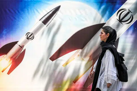 Seorang wanita berjalan melepasi sepanduk pelancaran peluru berpandu yang dipasang di tengah Teheran pada 15 April dalam kempen Iran memerangi Israel.