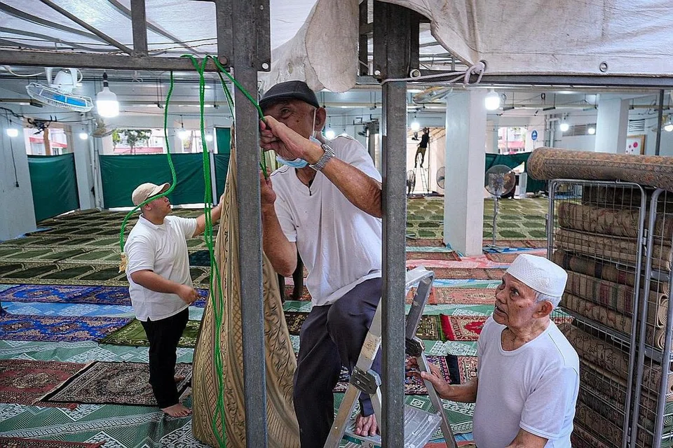 GOTONG-ROYONG: Encik Yassin (tengah) giat membuat persiapan bersama relawan lain di kolong Blok 450 Tampines Street 42 sebelum ketibaan jemaah bagi solat tarawih pada Rabu. - Foto BH oleh SHAFIQ APANDI