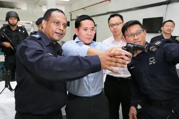 TUNJUK CARA GUNA PISTOL: Komander ProCom, Penolong Pesuruhjaya (AC) Manimaran Pushpanatan (depan, kiri), menunjukkan cara menggunakan pistol Taurus kepada Encik Amrin, sambil disaksikan Dr Tan (berkemeja merah jambu) dan Timbalan Penolong Pesuruhjaya (DAC) (NS) Ben Tan (depan, kanan). - Foto THE STRAITS TIMES
