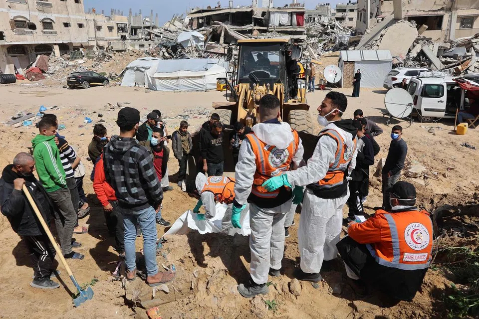 Pekerja pertahanan awam Palestin membongkar mayat yang dikebumikan di kawasan hospital Al-Shifa di Bandar Gaza pada 13 Mac.