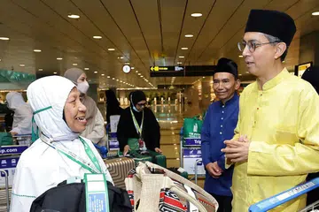 Pemangku Menteri Bertanggungjawab bagi Ehwal Masyarakat Islam, Profesor Madya Dr Muhammad Faishal Ibrahim (kanan), beramah mesra dengan salah seorang anggota jemaah haji yang tiba di Balai Ketibaan Terminal 3 Lapangan Terbang Changi pada 13 Jun, sambil diiringi Presiden Majlis Ugama Islam Singapura (Muis), Encik Saat Abdul Rahman (dua dari kanan).