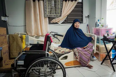 SENTIASA BERSYUKUR: Setelah kakinya dipotong, Cik Rose Enjong kini dijaga oleh cucu lelakinya sudah lebih 13 tahun. - Foto MUIS