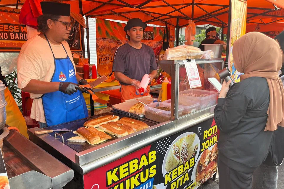 Pelanggan beratur untuk membeli roti john RM13 yang dijual Encik Syafaat Sasril, 31 tahun (kiri), di bazar Ramadan Kampung Baru, Kuala Lumpur, kerana keenakannya yang berbeza dengan roti john lain.