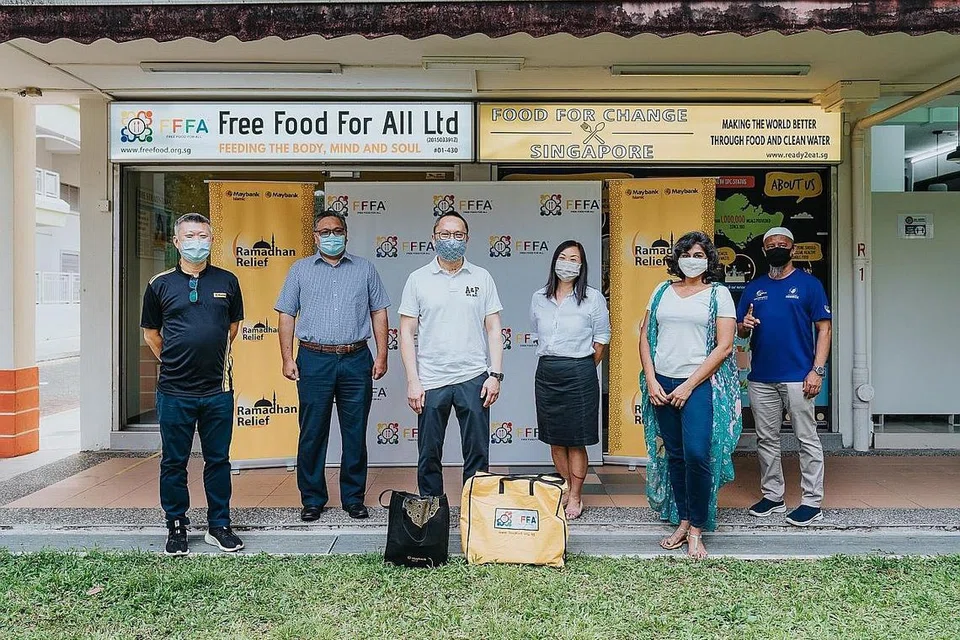 MEMBANTU GOLONGAN SUSAH: CEO Maybank Singapore, Dr John Lee (tengah, baju putih), bersama relawan (berbaju biru) yang memberikan bungkusan makanan kepada pekerja Malaysia di sini. - Foto MAYBANK