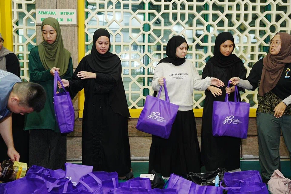 Cik Farra Nur Quraisya Irwan (tiga dari kiri) dan Cik Sofiyyatul Husna Habeeb Mohamed (tiga dari kanan) merupakan antara sekitar 100 belia yang membantu membungkus pek keperluan dapur untuk keluarga rentan di bawah inisiatif RamaDAWN, yang berlangsung di Masjid Kassim mulai sekitar 4 pagi pada 7 Mac.