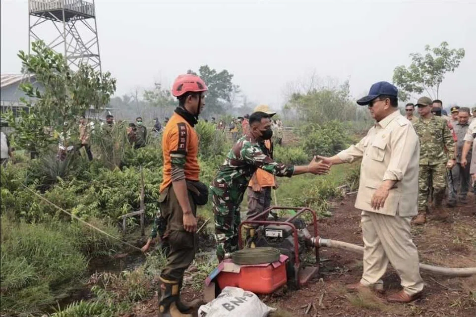Presiden Indonesia, Encik Prabowo Subianto (kanan), bersalaman dengan seorang anggota pasukan yang terlibat dalam operasi memadam kebakaran hutan dan tanah ketika meninjau kawasan terjejas di Kalimantan Barat pada 22 Ogos 2026. Lawatan itu dilakukan ketika kebakaran terus melanda beberapa wilayah di Kalimantan, mendorong pemerintah mengerahkan tiga batalion tambahan tentera membabitkan sekitar 1,500 anggota, enam helikopter berkapasiti besar bagi operasi pengeboman air serta menambah operasi pengubahsuaian cuaca, pam dan kerja penggerudian sumber air.