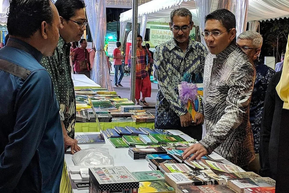 MEMASARKAN HASIL KARYA: Kamus turut serta dalam Pesta Buku Melayu Singapura pada tahun lalu di Wisma Geylang Serai dengan memasarkan buku-buku terbitannya. Kelihatan Dr Maliki Osman, Menteri Negara Kanan (Pertahanan merangkap Ehwal Luar ketika itu (kanan), melawat reruai Kamus. - Foto FACEBOOK/KAMUS