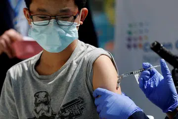 ATASI COVID-19: Seorang remaja kelihatan menerima suntikan vaksin Pfizer-BioNTech di New York selepas Amerika Syarikat meluluskan penggunaan vaksin itu ke atas golongan warga muda berusia 12 tahun hingga 15 tahun. Pihak berkuasa Singapura selepas membuat penelitian yang teliti juga baru-baru ini meluluskan penggunaan vaksin tersebut bagi golongan itu. - Foto REUTERS